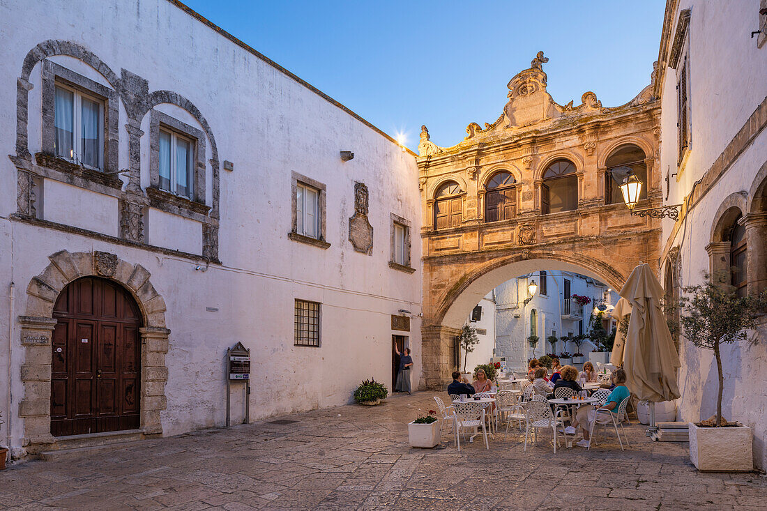 Arco Scoppa arch and Palazzo Vescovile and cafe in the Largo Arcid Teodoro Trinchera square in evening, Ostuni, Brindisi province, Puglia, Italy, Europe