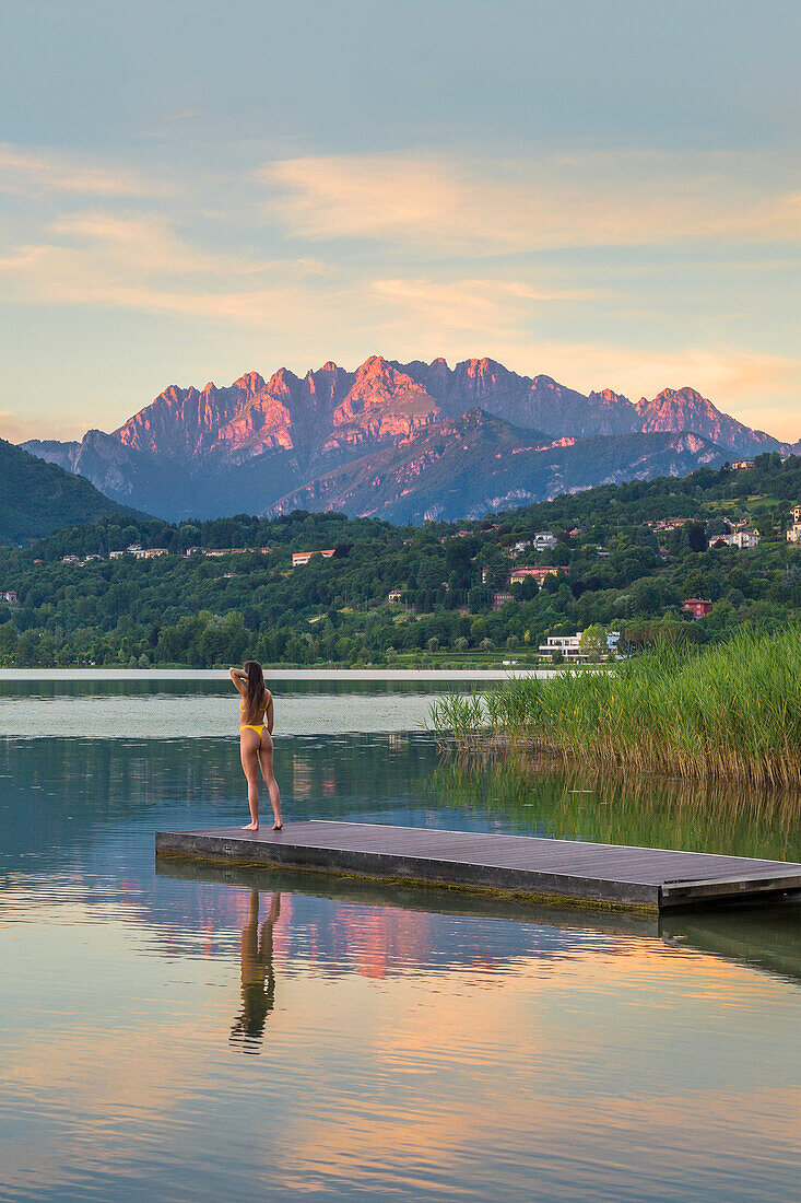 Girl relaxes and looks sunset on Resegone mount reflected into the Oggiono lake in summertime, Annone lake, Oggiono, Brianza, Lecco province, Lombardy, Italy, Europe (MR)