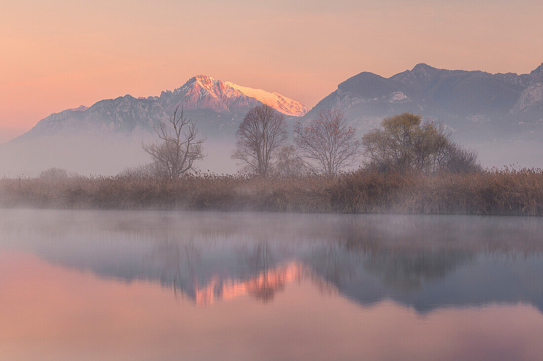 Foggy sunrise on Grigna Meridionale (Grignetta) reflected into the Adda river, Airuno, Lecco province, Lombardy, Italy, Europe