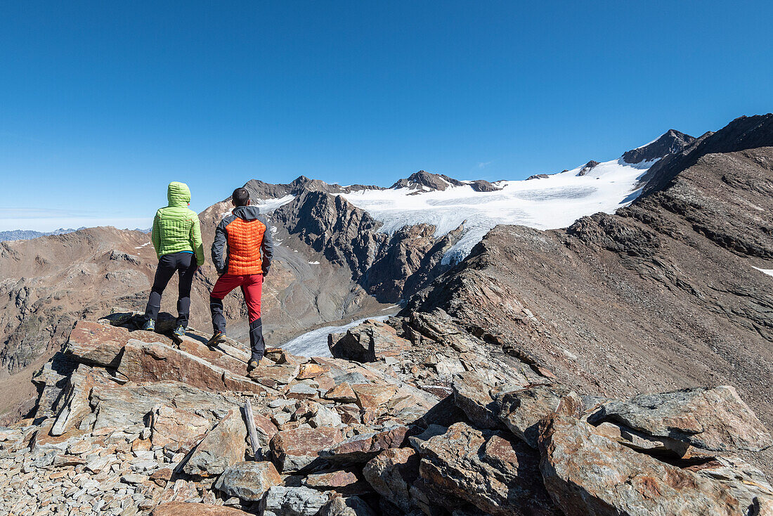 Couple of hikers admires the glacier of Dosegù from Piz Vallumbrina in Gavia Valley, Valtellina, Sondrio Province, Lombardy, Italy, Europe