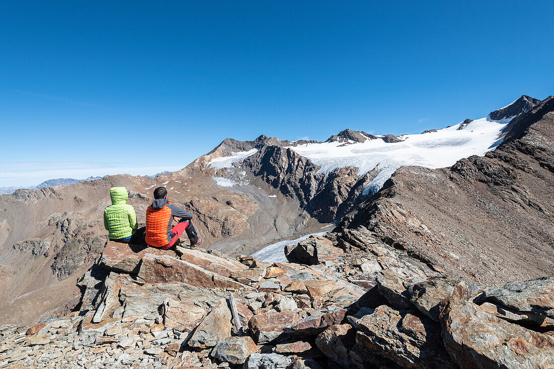 Couple of hikers admires the glacier of Dosegù from Piz Vallumbrina in Gavia Valley, Valtellina, Sondrio Province, Lombardy, Italy, Europe