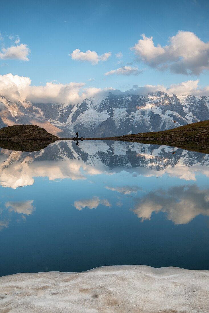 Man walks while Jungfrau Group is mirrored at Grauseeli lake, Murren, Lauterbrunnen, Switzerland, Europe