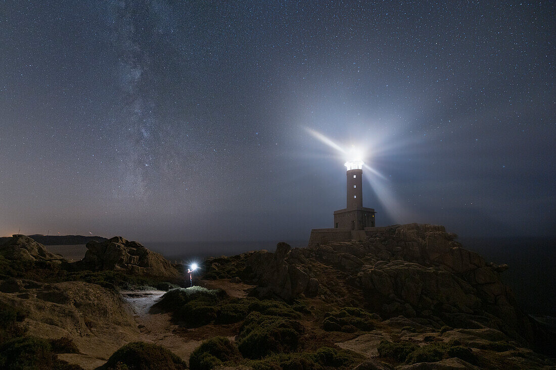 eine Person genießt die Milchstraße in der Nähe des Leuchtturms von Punta Nariga, während einer Sommernacht, Gemeinde Malpica de Bergantinos, Galixia, Spanien, Europa