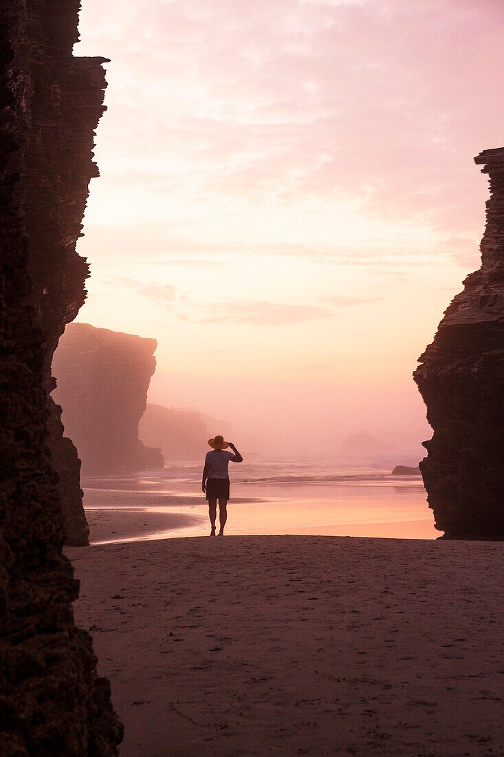 ein Tourist genießt den Sonnenuntergang während einer Ebbe am Praia de As Catedrais, Galixia, Spanien, Europa