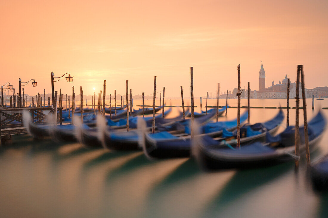 eine Langzeitbelichtung, um die Gondeln in der Nähe des Markusplatzes mit der Insel San Giorgio im Hintergrund bei Sonnenaufgang aufzunehmen, Gemeinde Venedig, Provinz Venedig, Region Venetien, Italien, Europa