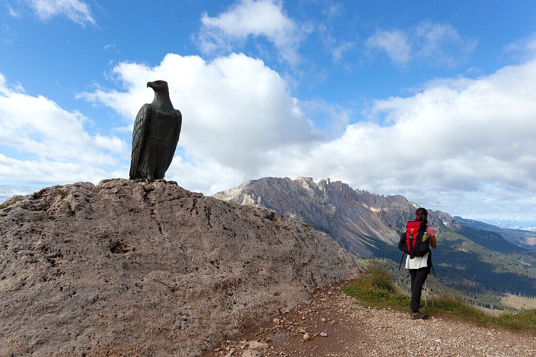 A hiker at Christomannos monument, with Latemar Group on the background, Dolomites, Catinaccio Group, Fassa Valley, Trento province, Trentino-Alto Adige, Italy