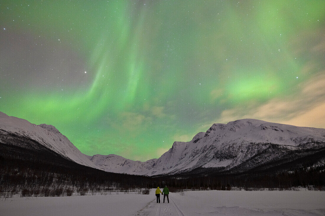 zwei Personen genießen das Spektakel der Nordlichter in einer kalten Winternacht, Troms, Norwegen, Europa