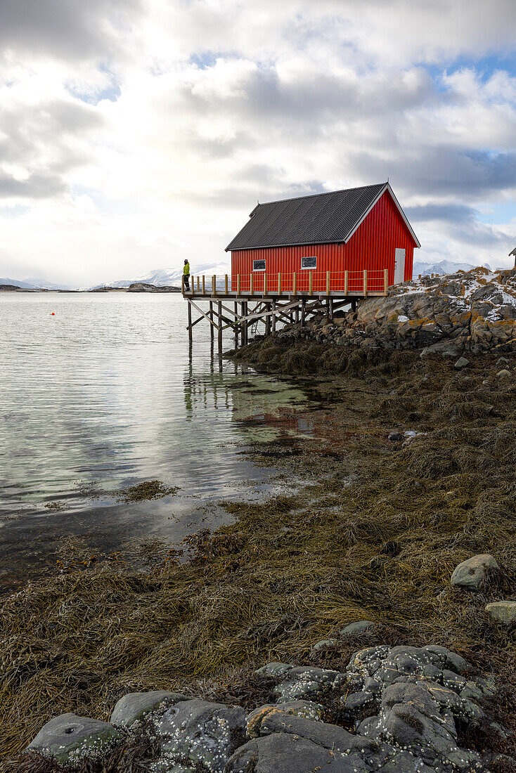 ein Tourist genießt den Panoramablick von einem klassischen Rorbuer an einem bewölkten Wintertag, Hillesoya, Troms, Norwegen, Europa