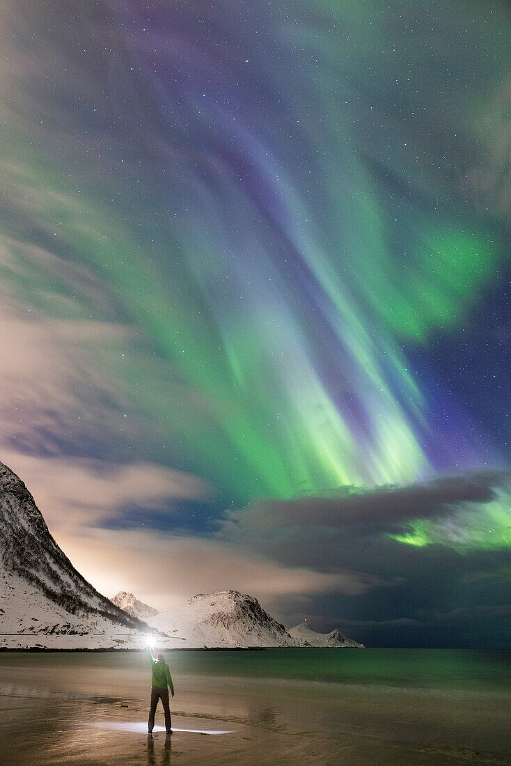 one person enjoy the magic of the arctic skies with the Northern Lights at Haukland beach, Lofoten island, Norway, Europe