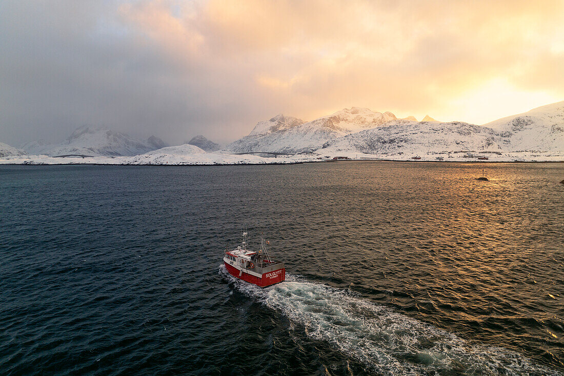 ein Fischerboot segelt in der Reine-Bucht während eines winterlichen Sonnenuntergangs, Lofoten, Norwegen, Europa
