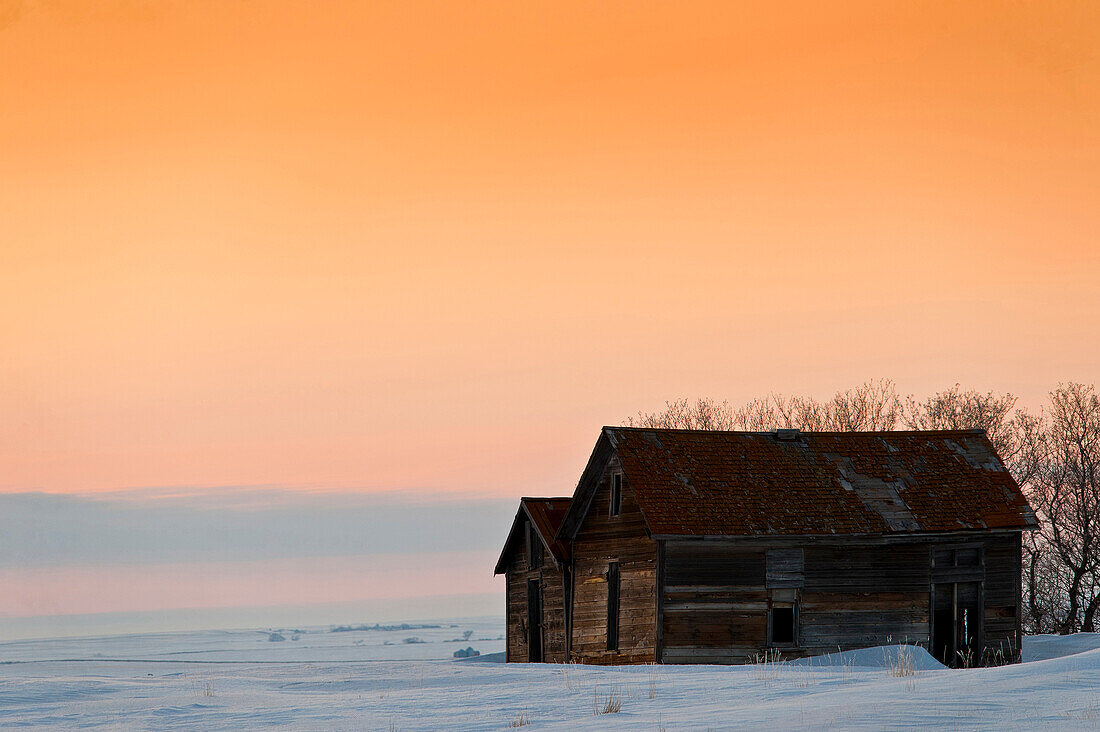 Old barns at prairie sunset in winter.