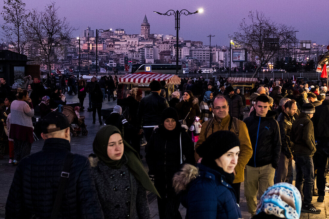 Spaziergänger in Eminönü, einem Viertel von Istanbul, nach Sonnenuntergang mit dem Galata-Turm im Hintergrund