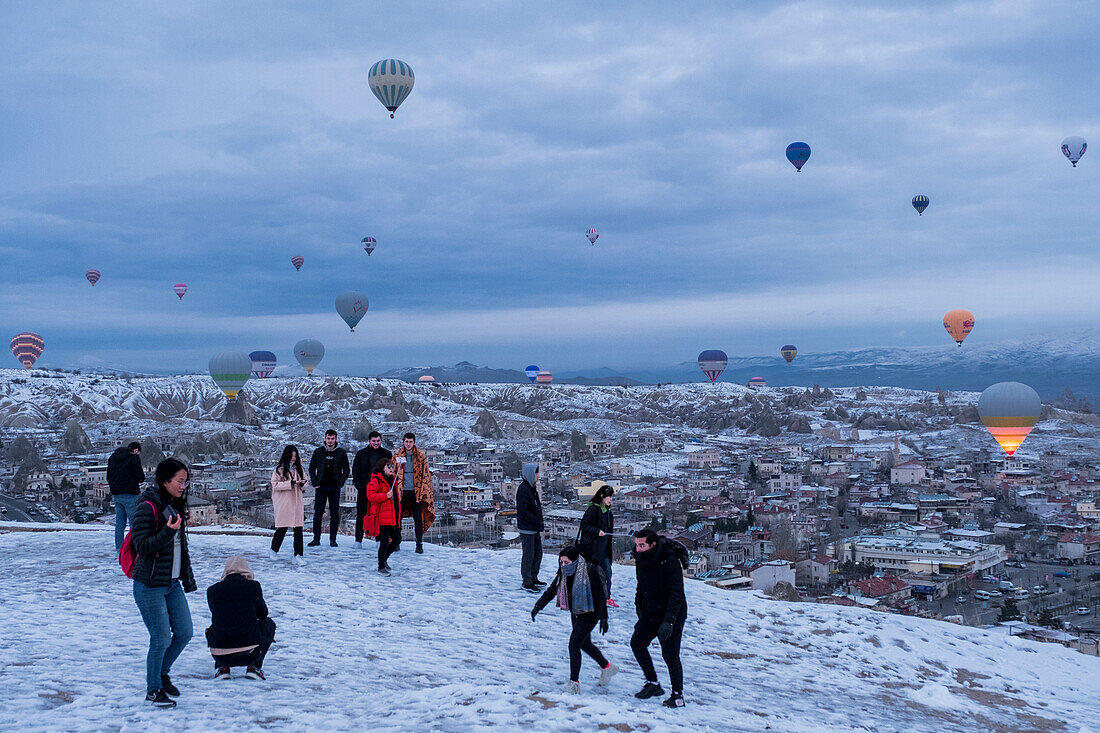 Cappadocia in winter covered with snow, tourists and hot-air balloon taking off near Göreme