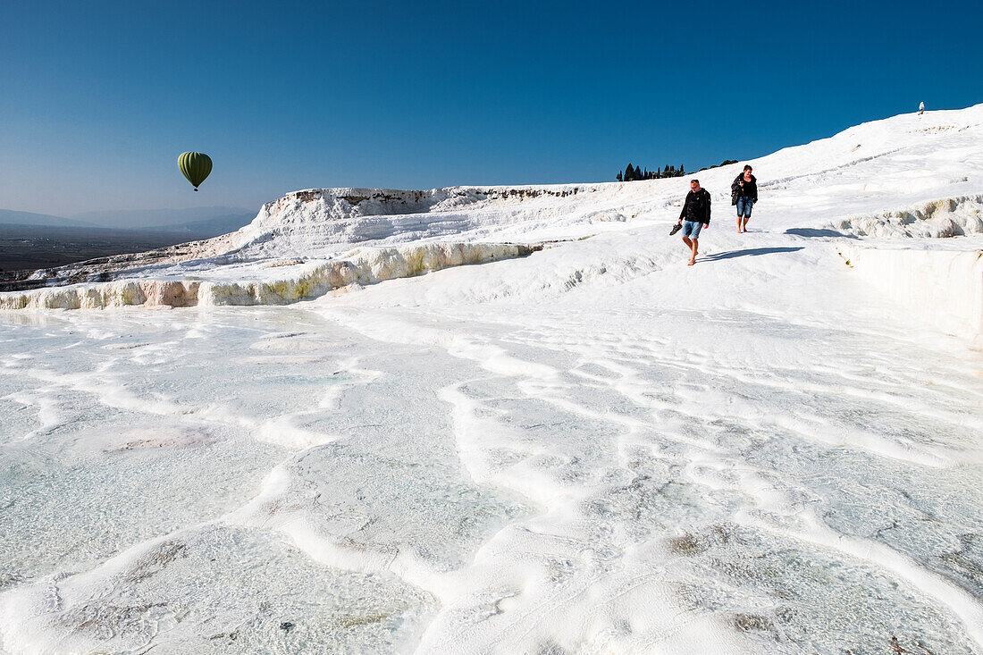 Travertine terrace formations at Pamukkale, tourists and hot-air balloon
