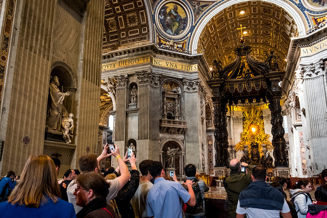 Touristen fotografieren den Baldachin des Heiligen Petrus im Inneren des Petersdoms