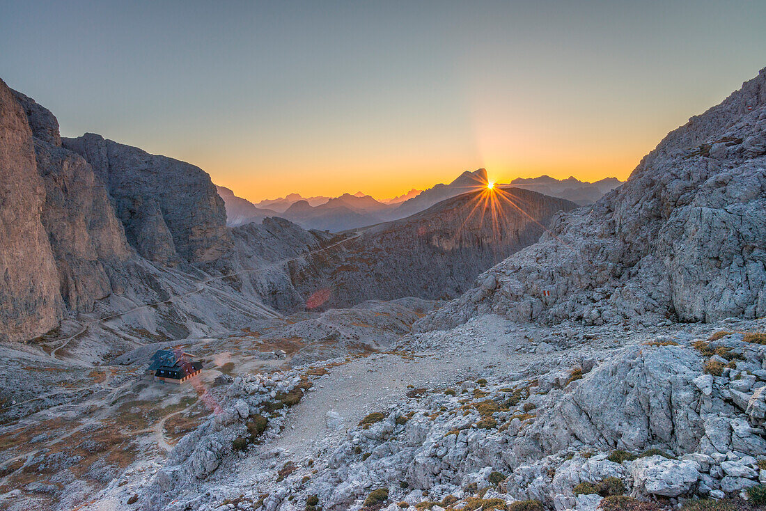 Mountain sunrise over Marmolada, sun rising behind mountains illuminating Antermoia hut. Belluno province, Veneto region, Italy.