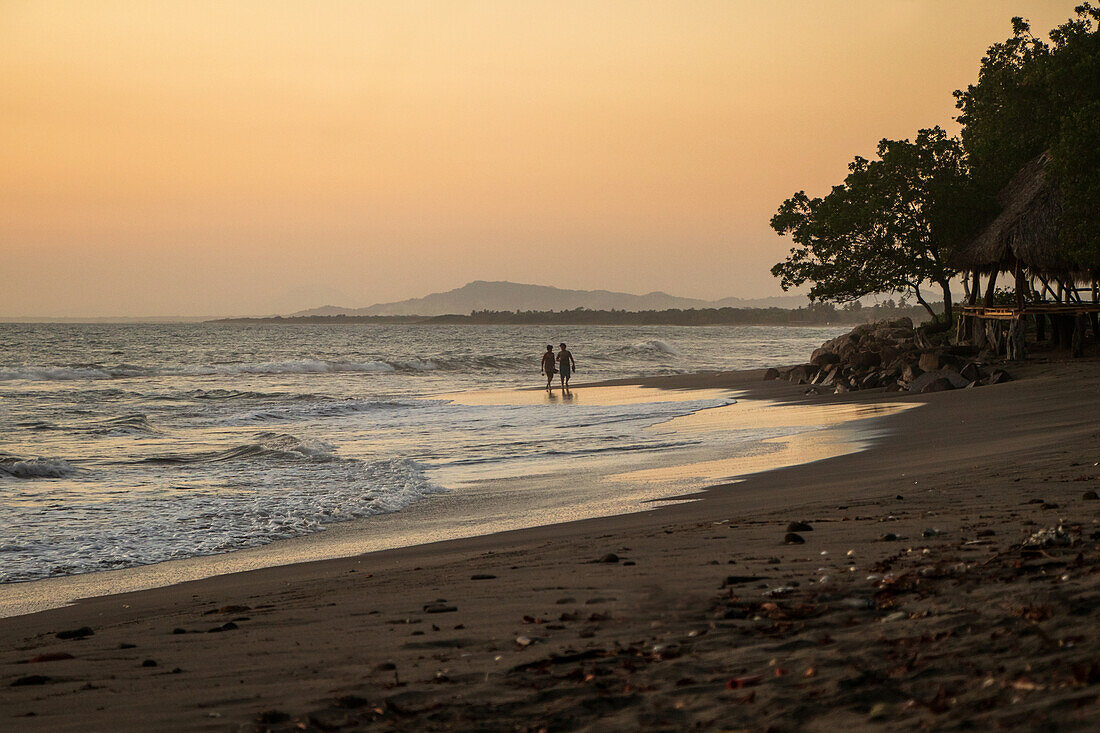Paar beim Spaziergang bei Sonnenuntergang am Strand von Jiquilillo, Chinandega, Nicaragua
