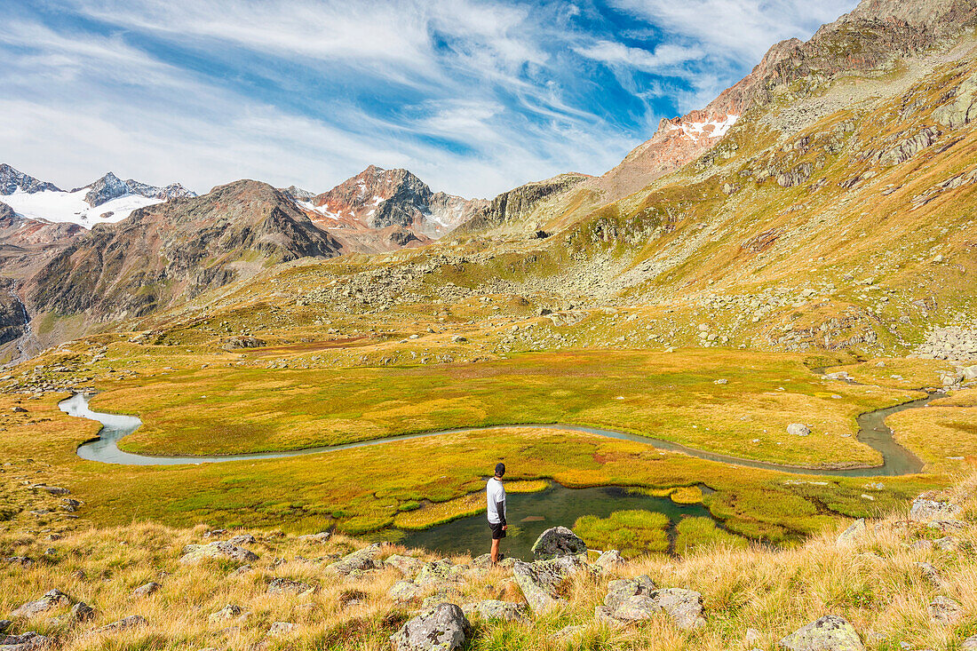 Ein Mann beobachtet einen Wildbach, der die Wiesen in der Nähe des Mutterbergersees durchquert, Stubaital, Innsbruck Land, Tirol, Österreich, Europa