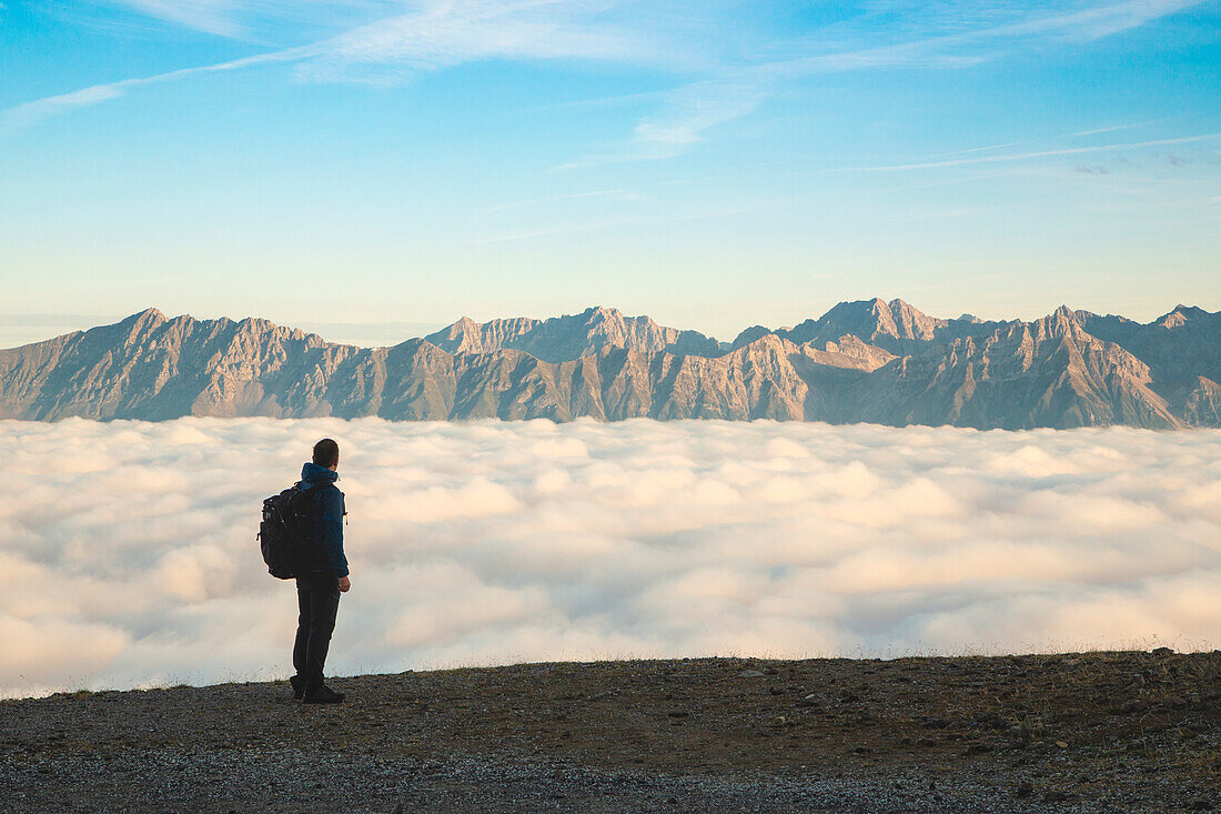 Ein Bergsteiger starrt auf das neblige Inntal mit den Bergen der Nordkette im Hintergrund, Patscherkofel, Innsbruck Land, Tirol, Österreich, Europa