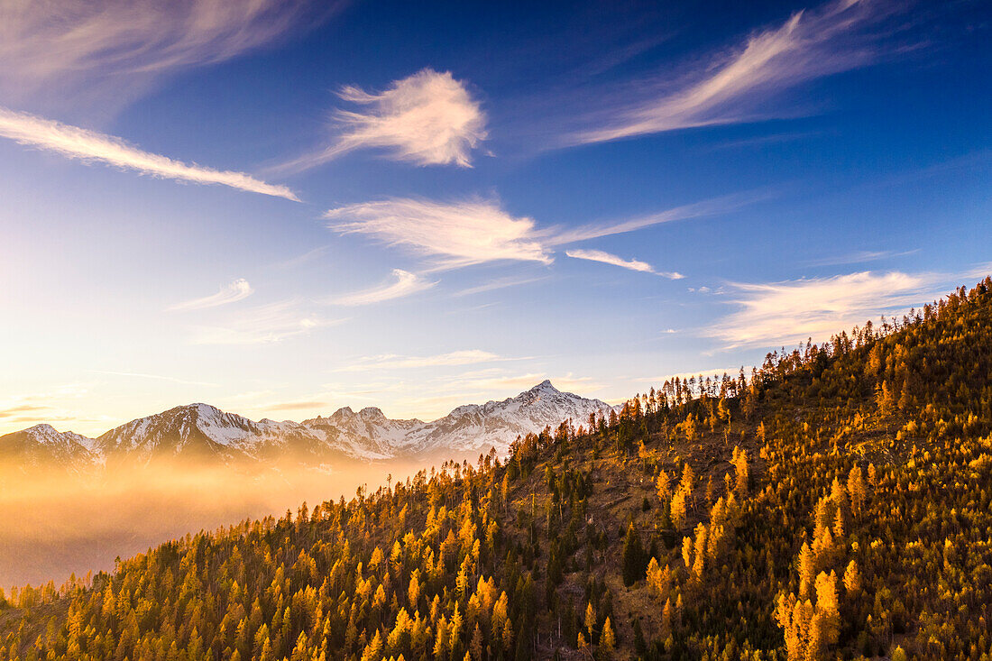 Sunlight illuminates fog, trees and clouds in autumn. Alpe Mara, Valtellina, Lombardy, Italy, Europe.