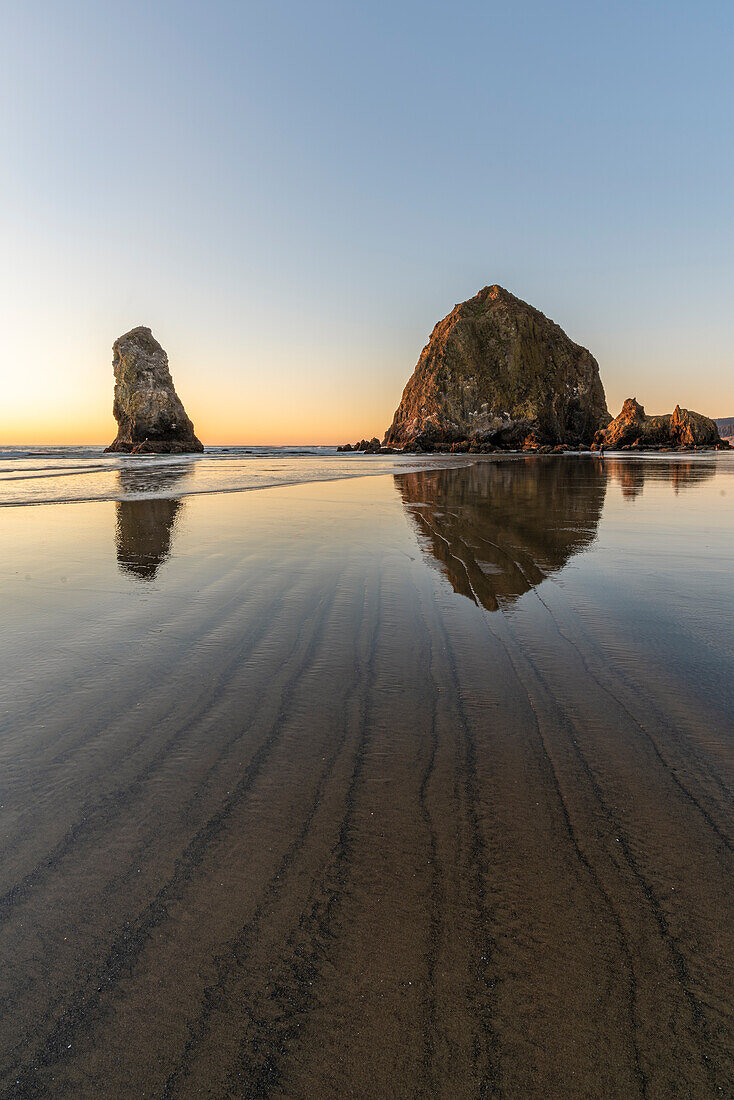 Haystack Rock und The Needles bei Sonnenuntergang, mit strukturiertem Sand im Vordergrund. Cannon Beach, Clatsop County, Oregon, USA.