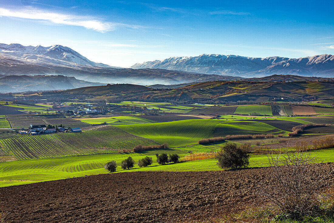 Hügellandschaft mit Wiesen, bewirtschafteten Feldern und kleinen Dörfern. Im Hintergrund die Bergketten des Maiella-Nationalparks. Abruzzen, Italien, Europa