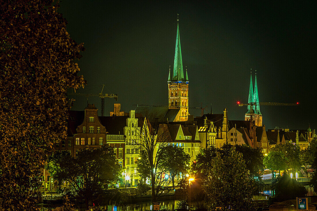 The bell towers of St. Peter's Church and the Cathedral of Lübeck, the ancient houses overlooking the river Trave illuminated by artificial lights on a summer evening. Lübeck, Land Schleswig-Holstein, Germany