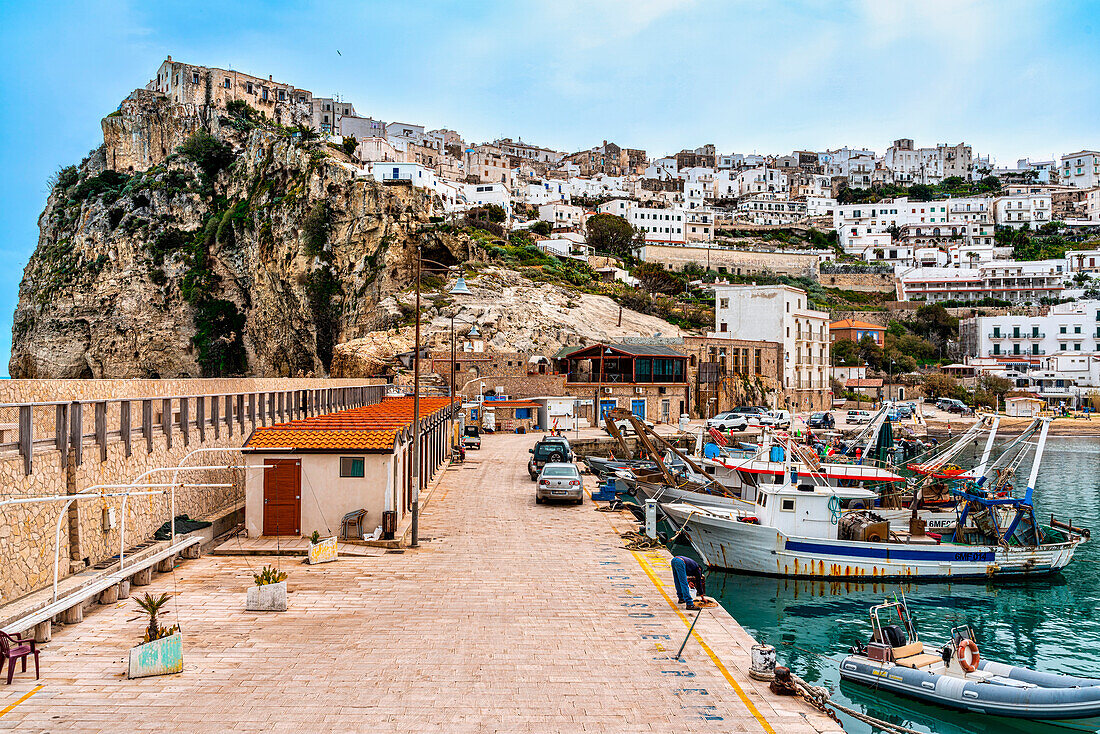 Port of Peschici, with the town perched on the cliff overlooking the sea and a ships anchored to the pier. Peschici, Foggia province, Puglia, Europe