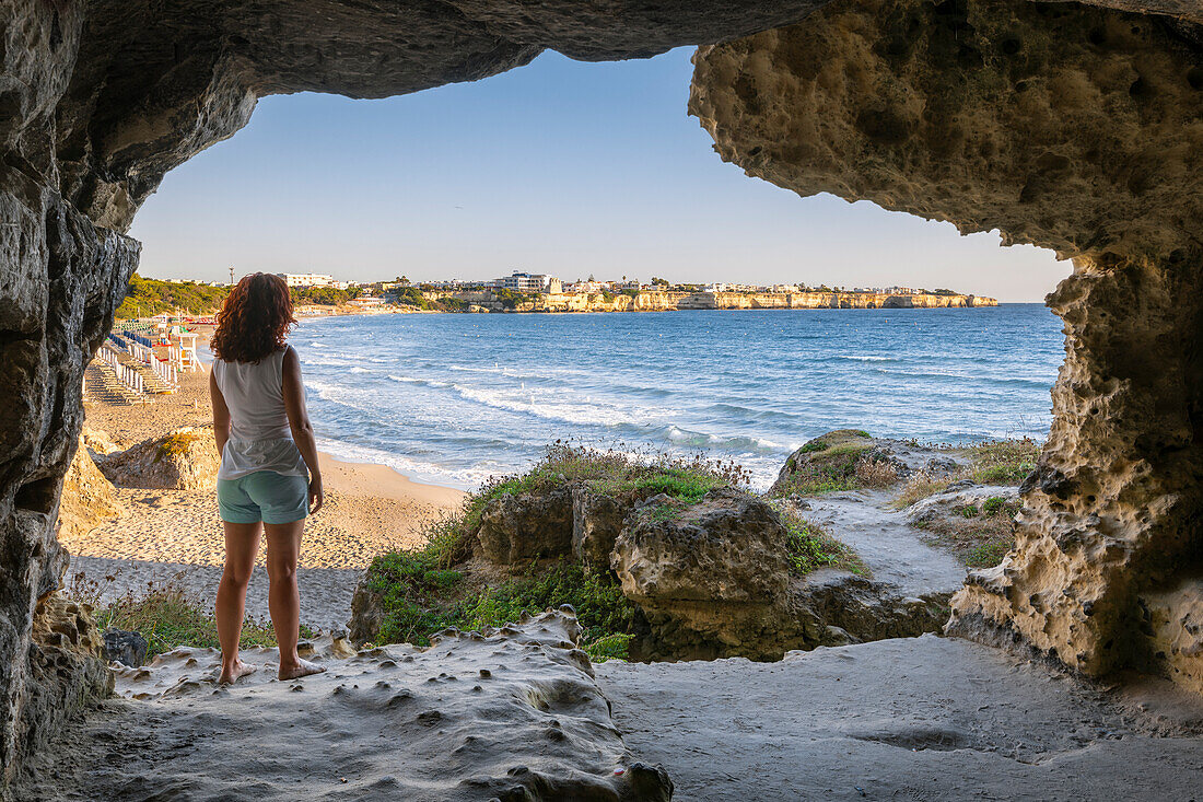 A young woman inside the San Cristoforo Cave in front of the Torre dell'Orso Beach (Torre dell'Orso, Melendugno, province of Lecce, Salento, Apulia, Italy) (MR)
