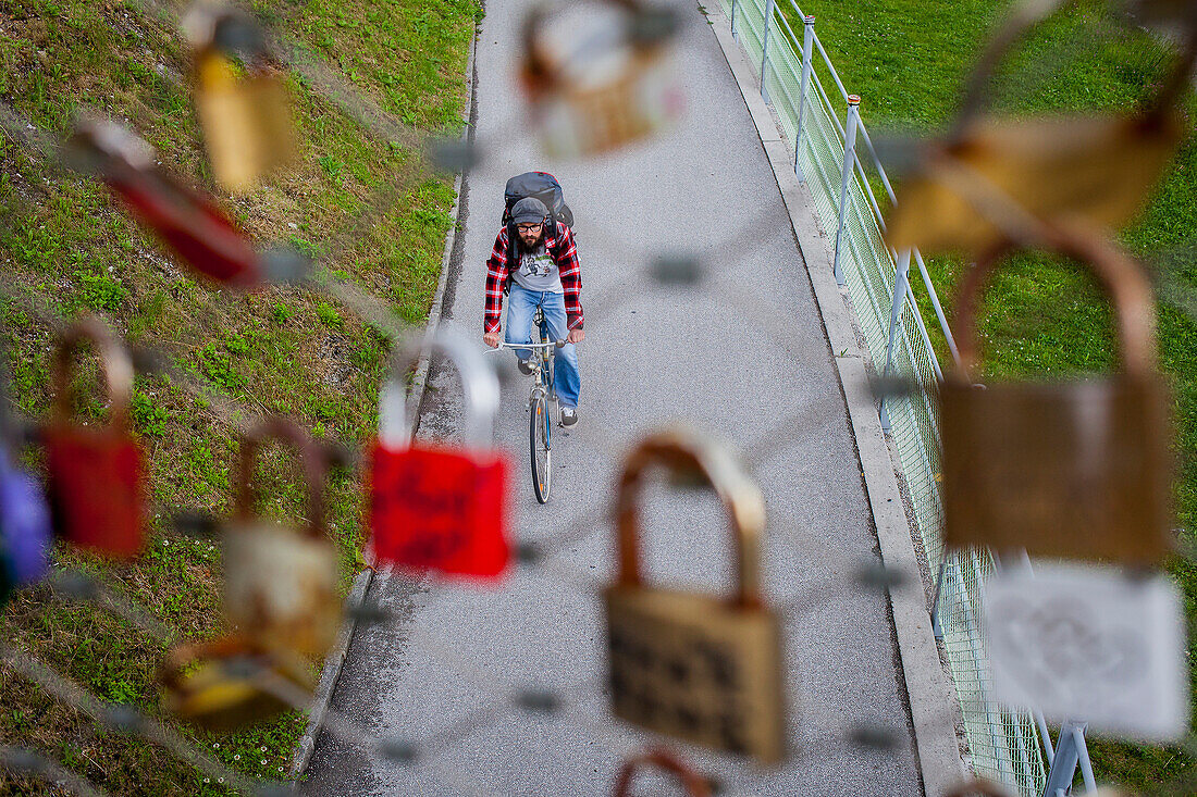 Radfahrer und symbolische Liebesvorhängeschlösser am Geländer der Makartsteg-Fußgängerbrücke, Salzburg, Österreich