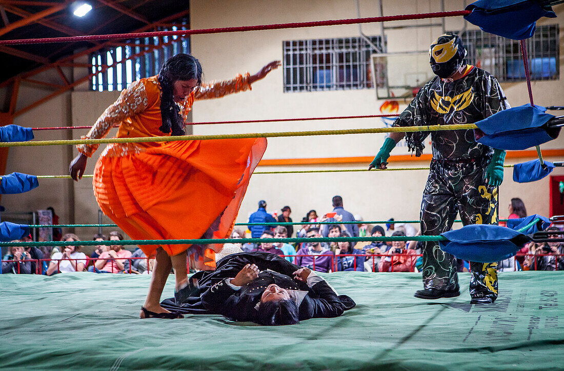 Lucha Libre. Kampf zwischen Dina mit orangem Kleid und Julieta, cholitas Wrestlerinnen, mit einem Schiedsrichter, Sportzentrum La Ceja, El Alto, La Paz, Bolivien