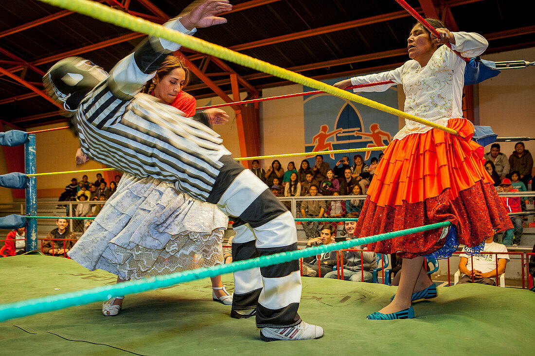 Lucha Libre. Kampf zwischen Dina mit orangenem Rock und Benita la Intocable, Cholitas Wrestlerinnen, mit Schiedsrichter in der Mitte, Sportzentrum La Ceja, El Alto, La Paz, Bolivien