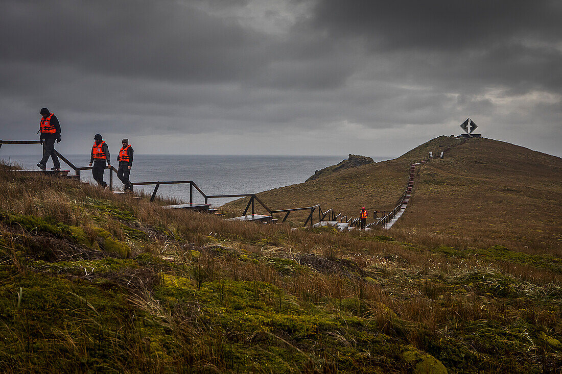 Explorers walking, in background Albatross memorial for lost mariners, Cape Horn, Tierra de Fuego, Patagonia, Chile