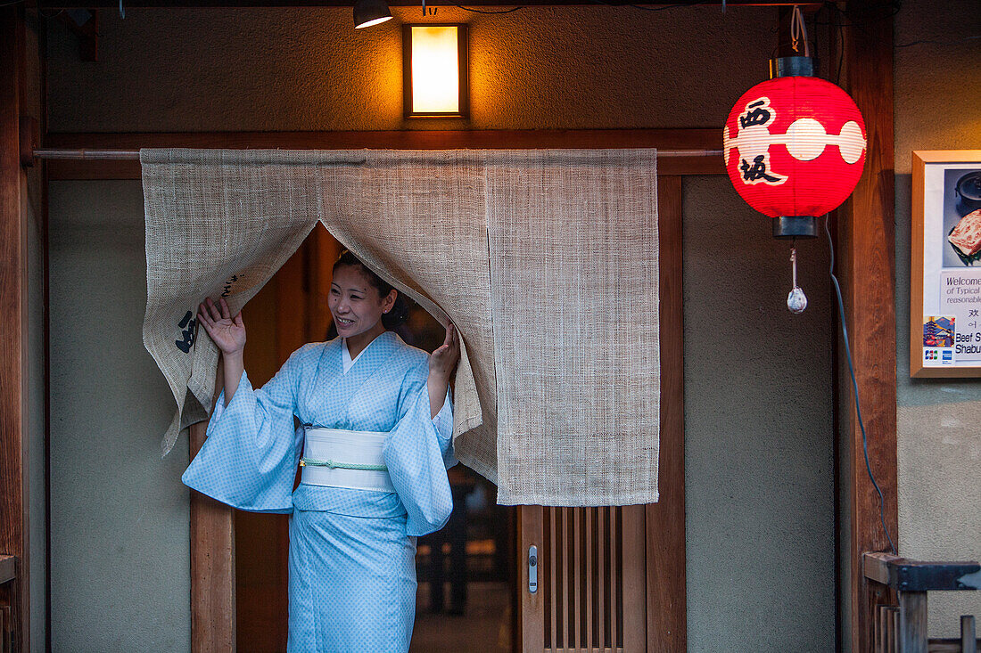 woman inviting passersby to enter into her restaurant.