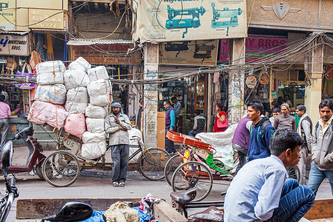 Carrier, resting and chatting through phone, in Nai Sarak street, near Chandni Chowk, Old Delhi, India