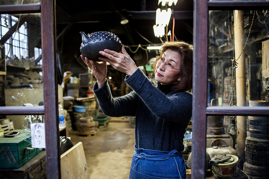 Morihisa Suzuki prüft die Qualität der Arbeit an einer neuen eisernen Teekanne oder Tetsubin, die einzige Frau, die in der fast 400-jährigen Geschichte des Eisenhandwerks in Iwate eiserne Teekannen hergestellt hat, in der Werkstatt von Morihisha Suzuki, Handwerker seit 1625, nanbu tekki, Morioka, Präfektur Iwate, Japan
