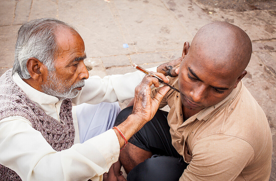 Barbier rasiert Kopf und Bart eines Pilgers, Dashashwamedh ghat (main ghat), im Fluss Ganges, Varanasi, Uttar Pradesh, Indien.