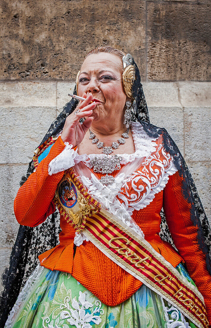 Woman smoking in Fallera Costume during Flower offering parade, tribute to `Virgen de los desamparados´, Fallas festival, Plaza de la Virgen square,Valencia