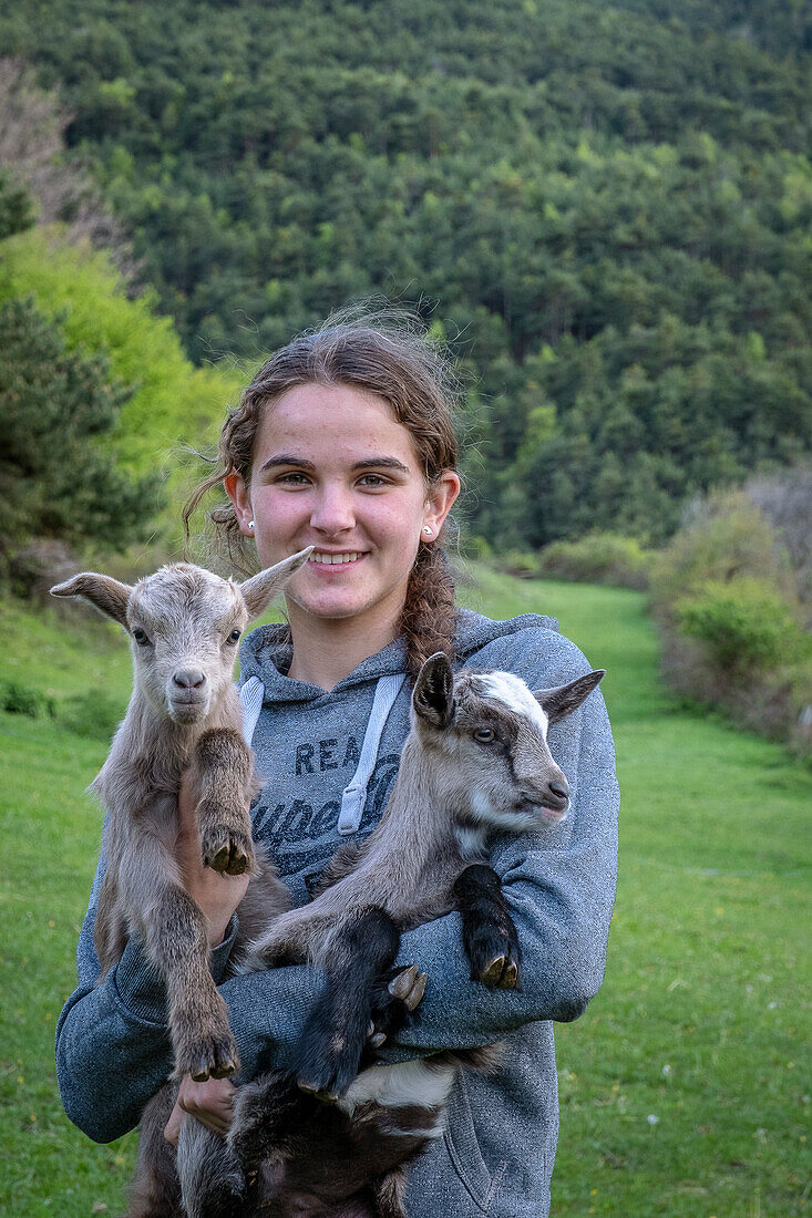 Janira posiert mit einem Zicklein. Tägliches Leben in einem traditionellen Bauernhof in den Bergen, Dorf Roni, Naturpark Alt Pirineu, Lleida, Katalonien, Spanien