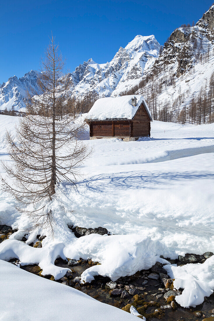 Blick auf Berghütten in der Nähe des Wildbachs Devero in der kleinen Stadt Crampiolo im Winter. Alpe Devero, Antigorio-Tal, Piemont, Italien.