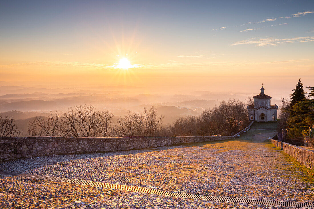 View of the last chapel of the Sacro Monte di Varese with the fog on the Pianura Padana at sunrise. Sacro Monte of Varese. Varese, Lombardy, Italy.