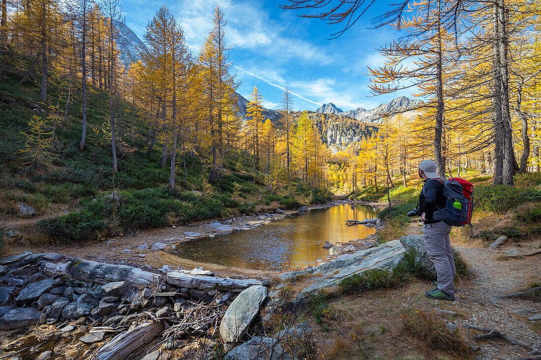 Autumnal view of an hiker admiring the colours and reflections at Lago delle Streghe. Alpe Veglia, Val Cairasca valley, Divedro valley, Ossola valley, Varzo, Piedmont, Italy.