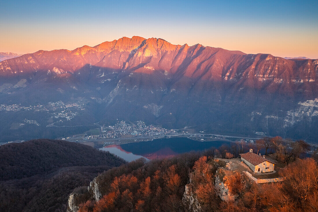 View of the small church at the top of Monte San Giorgio with Monte Generoso at sunset. Monte San Giorgio, Brusino Arsizio, Canton Ticino, Switzerland.