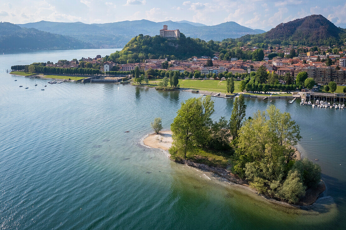 Blick auf die Stadt Angera und ihre Festung, die Rocca di Angera, an einem Frühlingstag mit der kleinen Insel Isolino Partegora. Angera, Lago Maggiore, Bezirk Varese, Lombardei, Italien.