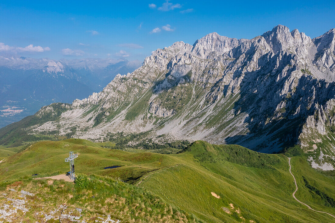 Luftaufnahme des Kreuzes auf dem Gipfel des Monte Campioncino in Richtung Valcamonica und Concarena im Frühling. Cerveno, Val Camonica, Bezirk Brescia, Lombardei, Italien, Südeuropa.