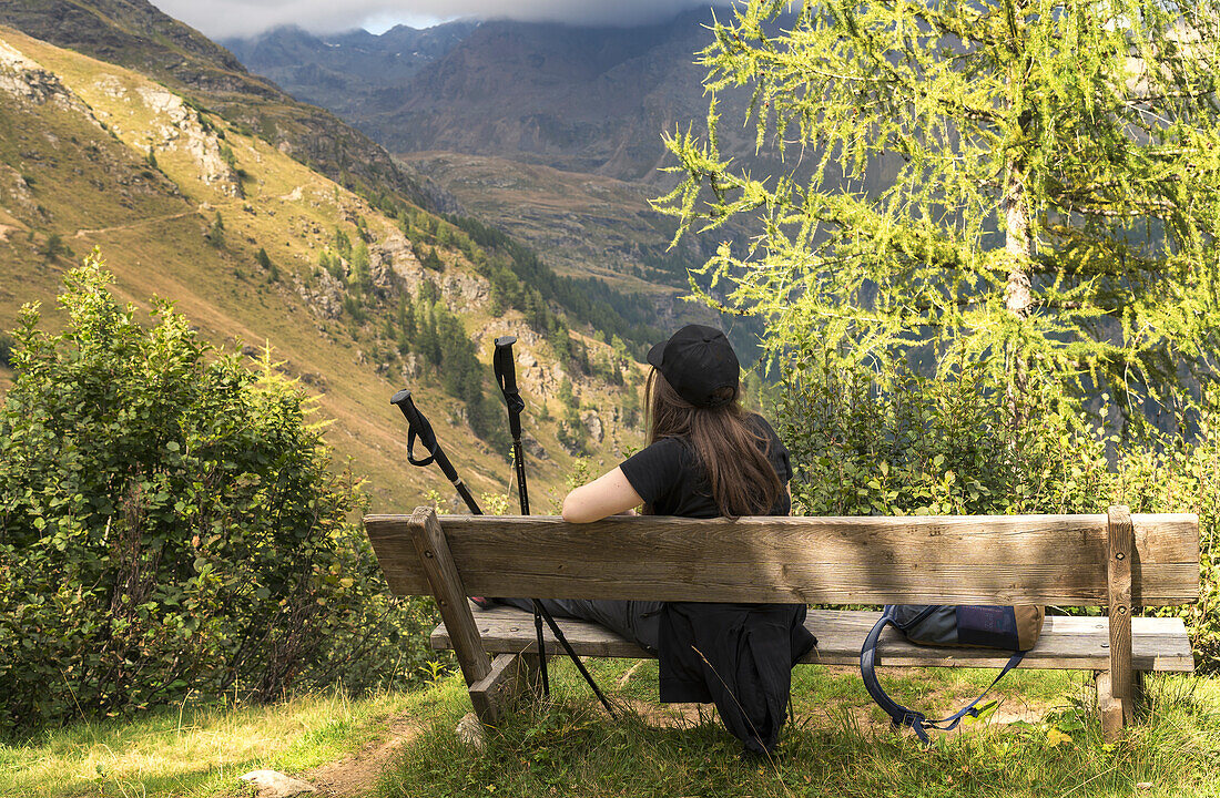 A young girl is resting on a benche along a footpath, Bagni di Rabbi, Rabbi, Rabbi Valley, Autonomous Province of Trento, Trentino Alto-Adige/Sudtirol, Italy