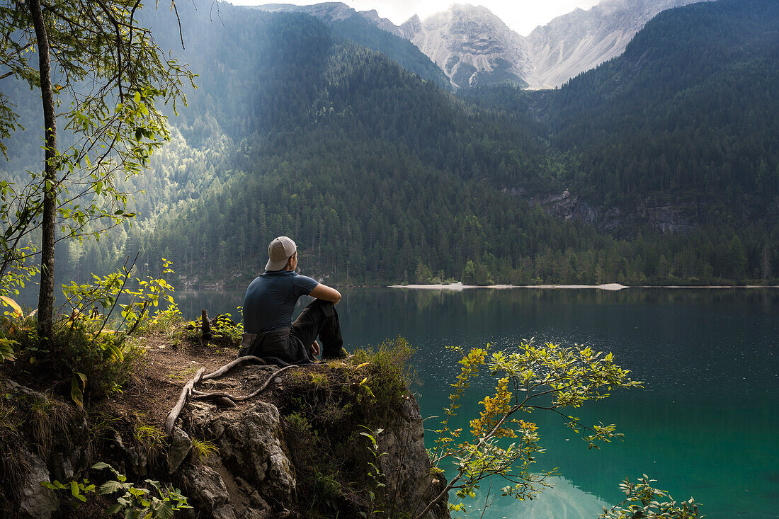 A young man sitting on a rock and admire the scenery, Lake Tovel, Ville d'Anaunia, Non valley, Trentino, Trento Province, Trentino-Alto Adige, Italy, Europe