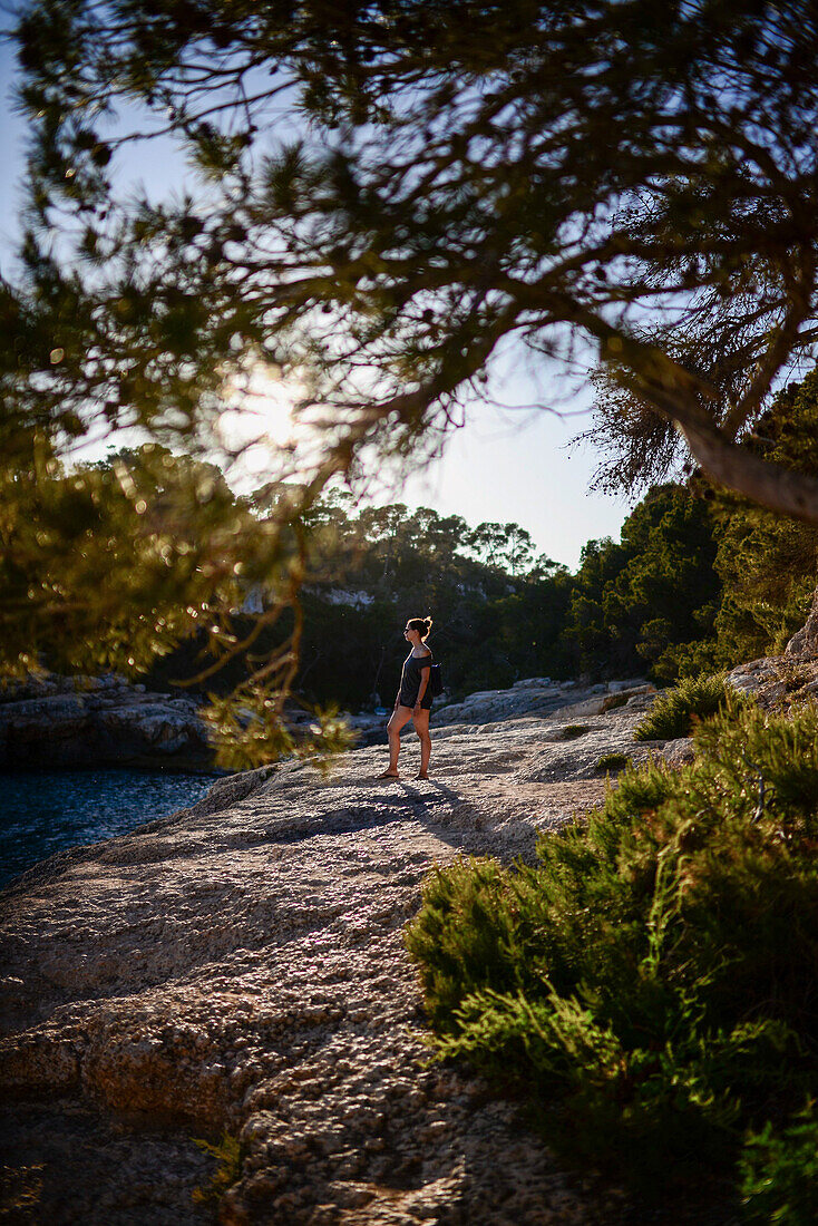 Young woman, surrounded by nature, looking at the horizon at sunset in the coast of Mallorca, Spain