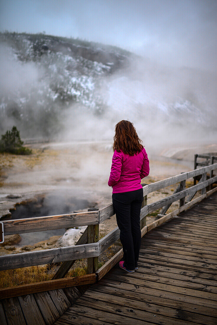 Junge Frau betrachtet einen Geysir im Yellowstone-Nationalpark, USA