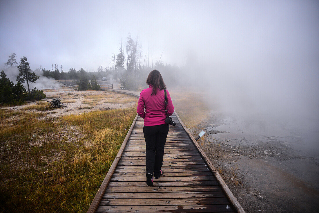 Junge Frau geht auf einem Holzpfad im Yellowstone-Nationalpark, USA